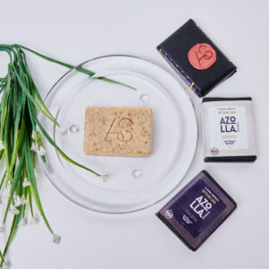 3 Wrapped bathing soap, to the left of a glass plate with an unwrapped bathing bar in the centre