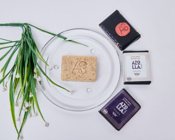 3 Wrapped bathing soap, to the left of a glass plate with an unwrapped bathing bar in the centre